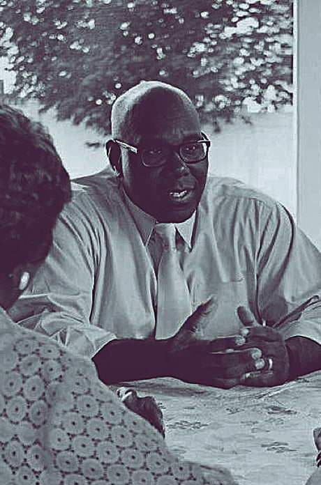 A black and white closeup of a legislator speaking to others at a table.